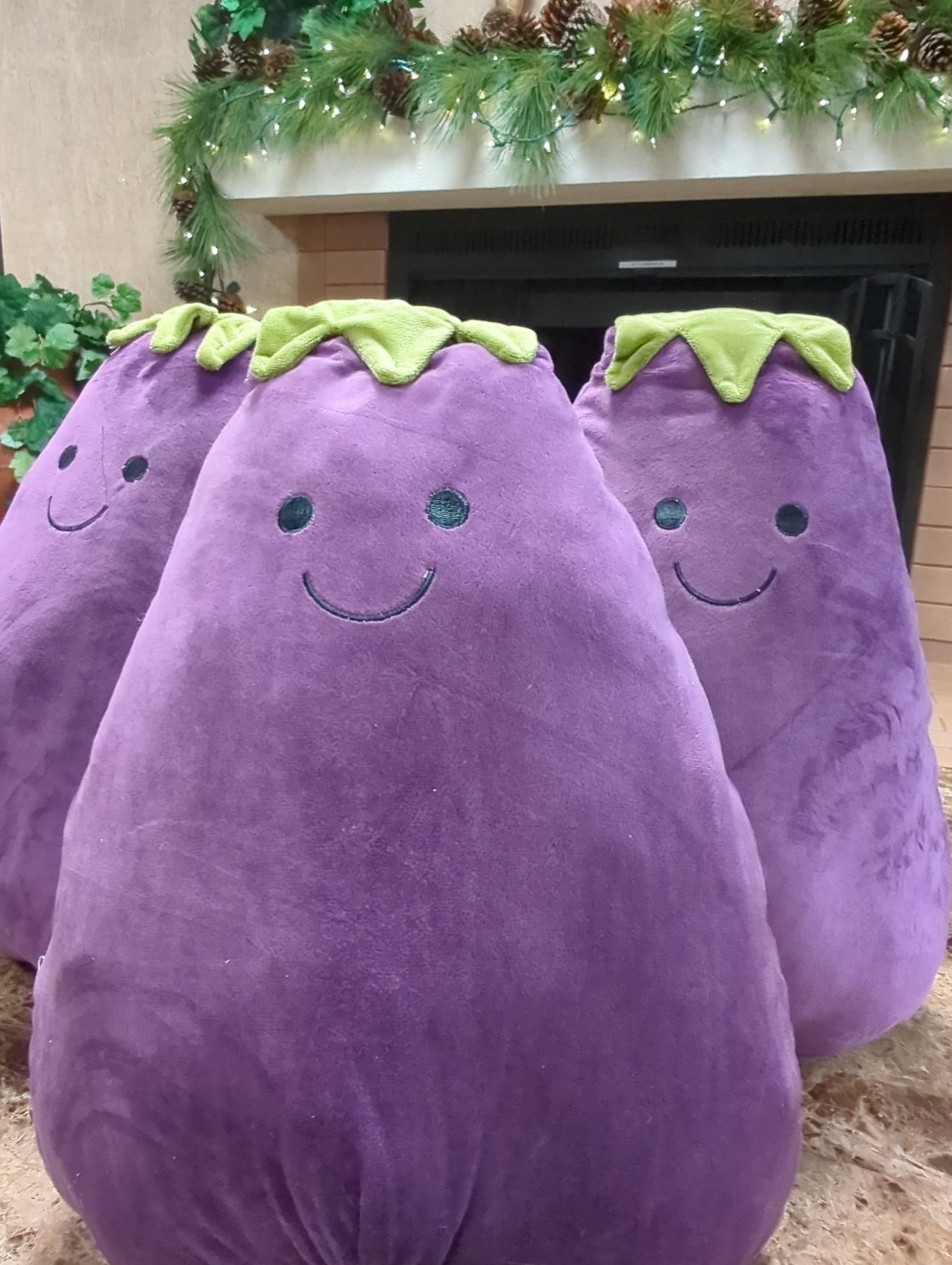 three purple plush eggplants with green stems against a stone wall.